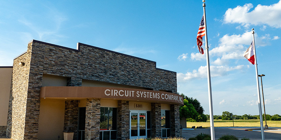Exterior of Circuit Systems building with brick facade and two flags.
