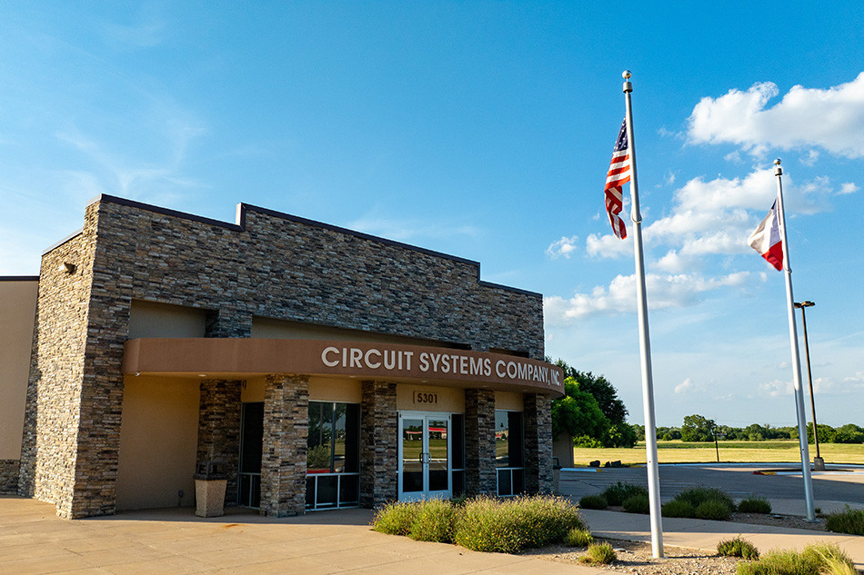 Exterior of Circuit Systems building with brick facade and two flags.