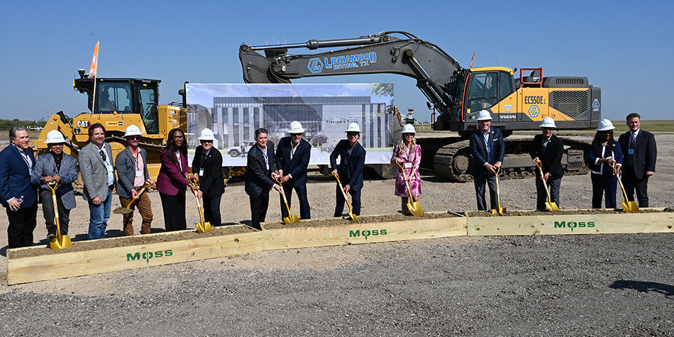 A line of people with golden shovels and hard hats in front of a bulldozer