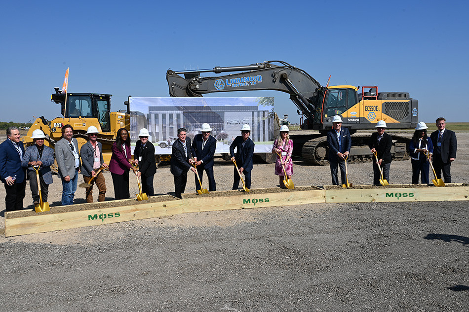 A line of people with golden shovels and hard hats in front of a bulldozer