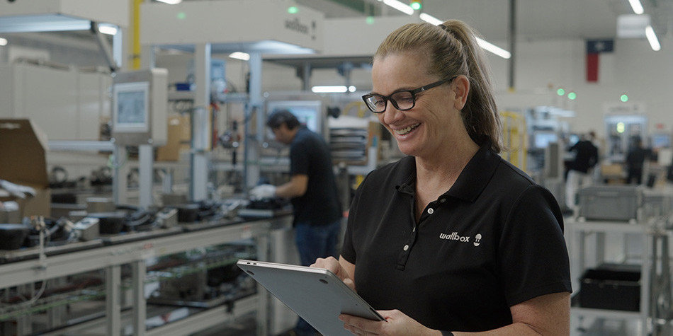 Woman in a manufacturing facility smiling and looking down at iPad