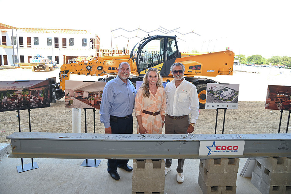 Two men and a woman standing behind the final beam for Caravan Court Hotel, in front of a bulldozer